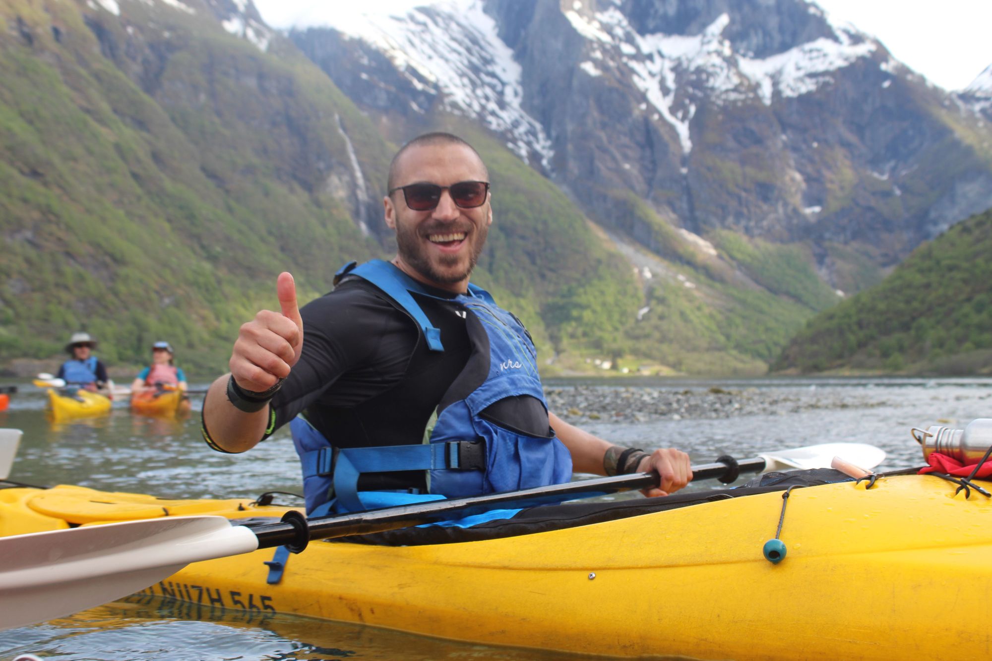 Un uomo posa con il pollice alzato su un kayak nei fiordi norvegesi.